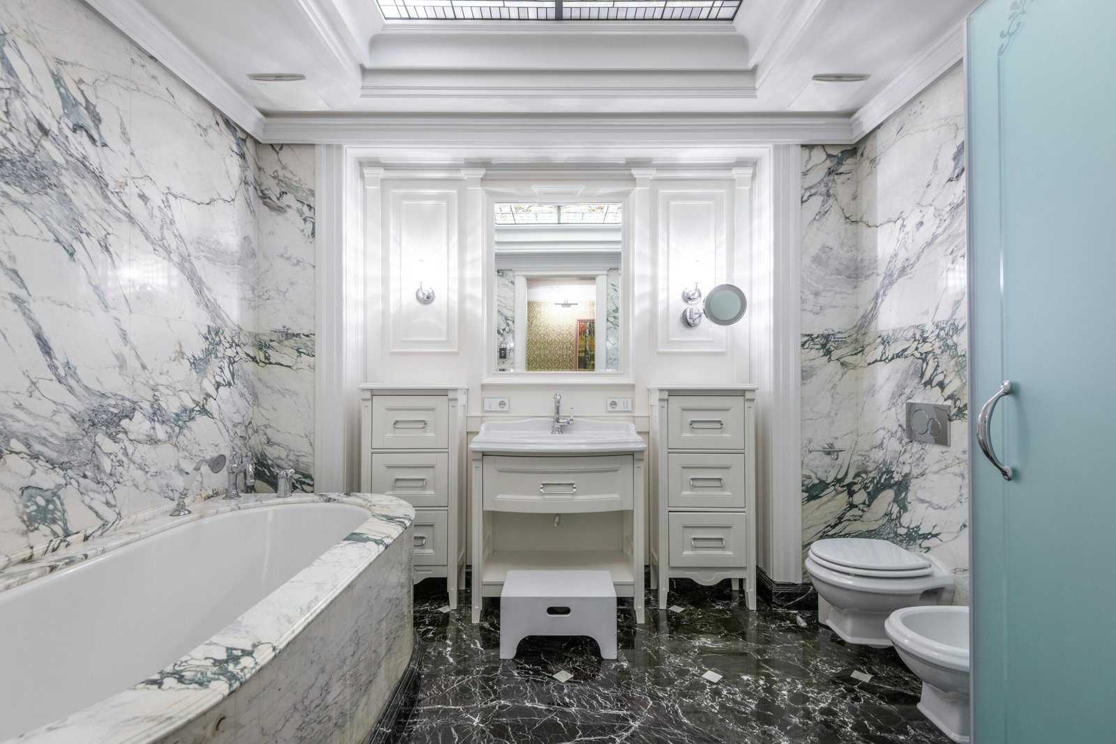 Bathroom lined in veined white marble with a dark marble floor